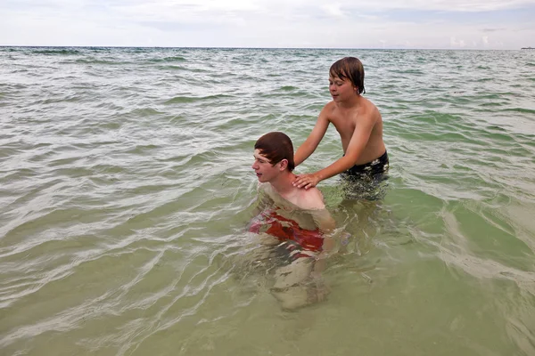 Jongens hebben plezier in de mooie heldere zee door pickaback te spelen — Stockfoto