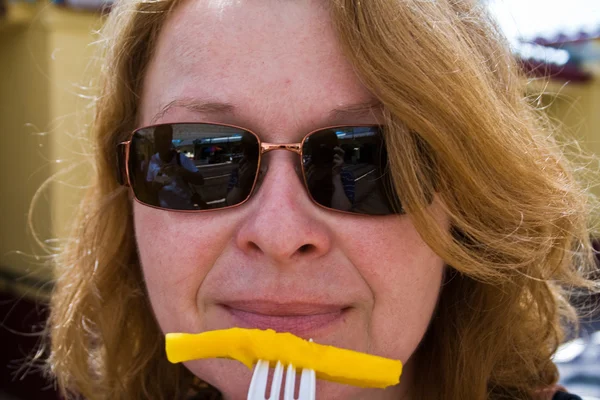 Smiling woman with french fries on a plastic fork — Stock Photo, Image
