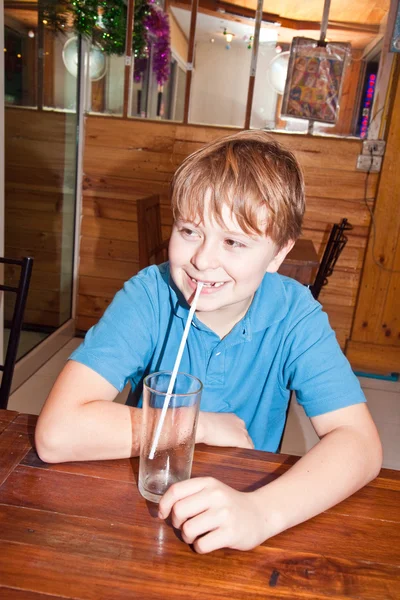 Jongen zittend in een restaurant en een rietje gebruiken om te drinken — Stockfoto