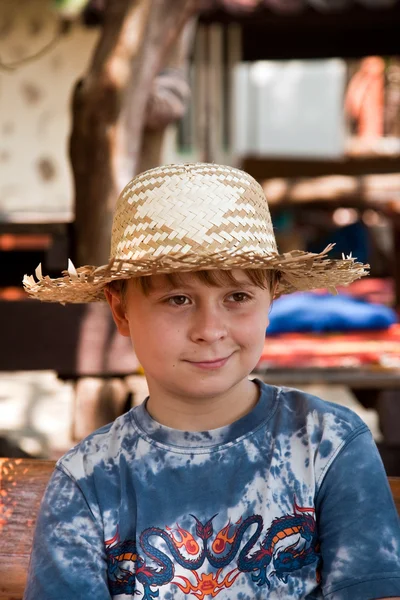 Boy with straw hat has a rest in the sun at an open air restaura — Stock Photo, Image