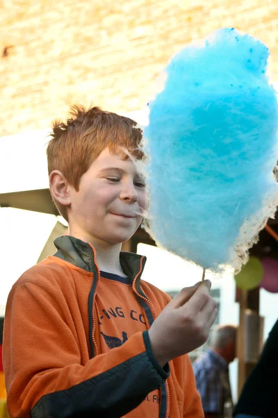 Boy enjoys cotton candy at the fair and licks his hands — Stock Photo, Image