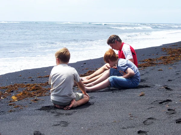 Família está coletando pedras preciosas na praia negra vulcânica em La — Fotografia de Stock