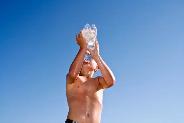 Мальчик пьет воду на пляже — стоковое фото