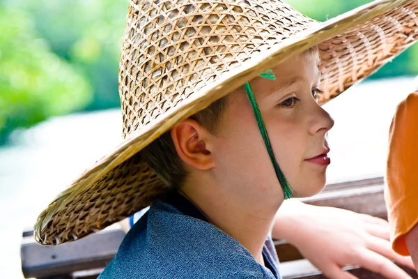 Niño lleva un sombrero de bambú durante un viaje en barco —  Fotos de Stock