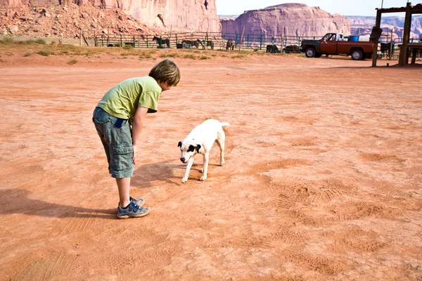 Monument Valley, chico acaricia a un hermoso perro encantador en las tierras —  Fotos de Stock
