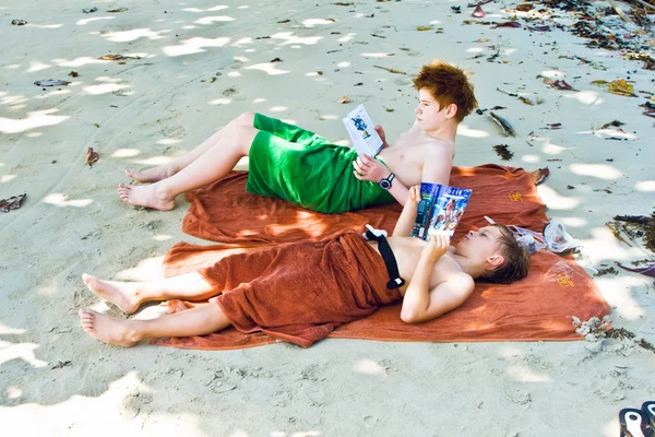 Hermanos están tumbados en la playa de arena en la sombra, relajando un —  Fotos de Stock