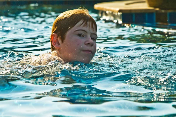 Boy with red hair is swimming in the pool and enjoys the fresh w — Stock Photo, Image