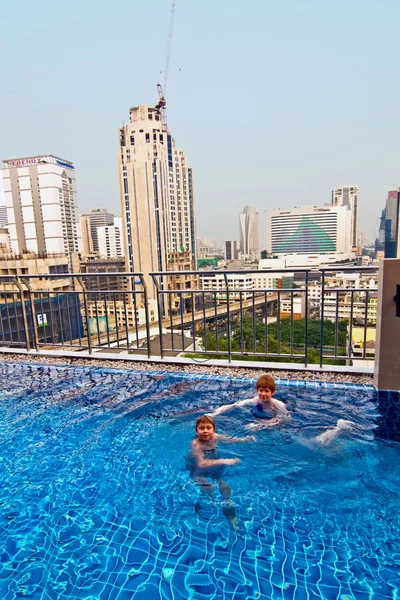 Chłopcy są pływanie w powietrzu basen z pięknym widokiem na wieżowiec — Zdjęcie stockowe
