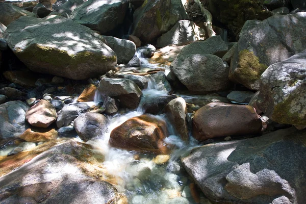 Piedras coloridas en el agua fría clara de un arroyo con agua de yosemite —  Fotos de Stock