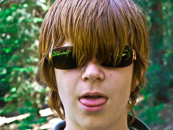 Young boy with red long hair and sunglasses pocks his tongue and looks real — Stock Photo, Image