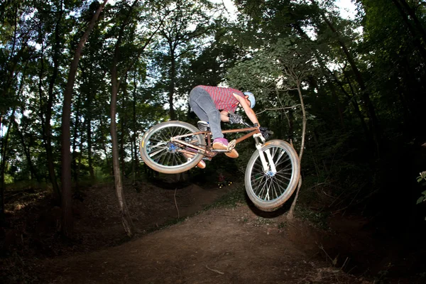 Lindo adolescente saltando con su bicicleta sobre una rampa natural en los frentes — Foto de Stock