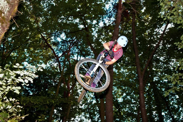 Cute teen jumping with his bike over a natural ramp in the fores — Stock Photo, Image