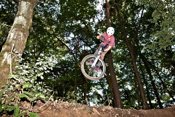 Adolescente bonito pulando com sua bicicleta sobre uma rampa natural nos inimigos — Fotografia de Stock
