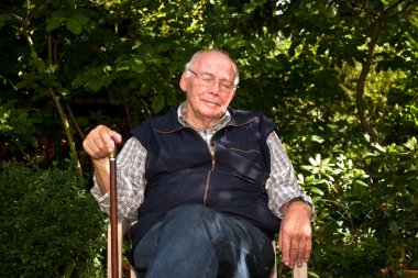 Portrait of elderly man sitting happy in his garden with closed