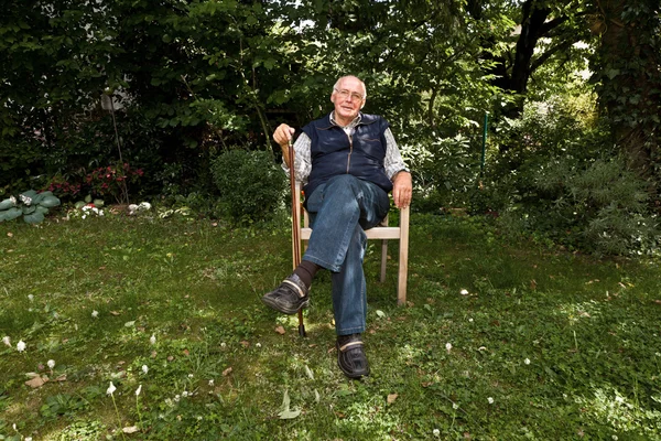 Porträt eines älteren Mannes, der glücklich in seinem Garten sitzt — Stockfoto