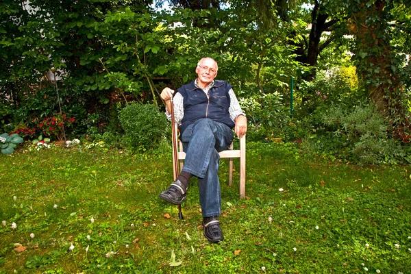 Portrait of elderly man sitting happy in his garden — Stock Photo, Image