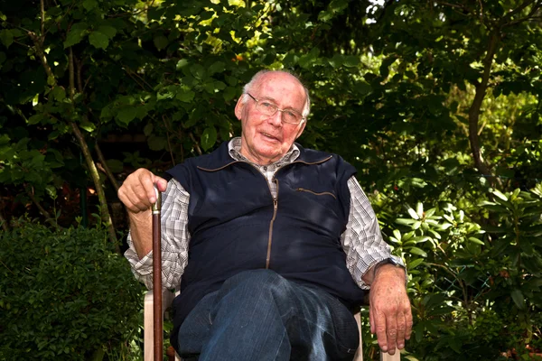 Porträt eines älteren Mannes, der glücklich in seinem Garten sitzt — Stockfoto