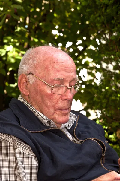 Homem idoso sentado em uma cadeira em seu jardim e parece pensativo — Fotografia de Stock