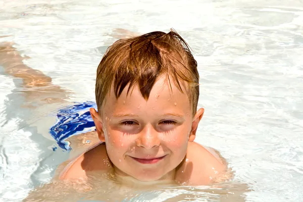 微笑着的年轻男孩喜欢躺在游泳池 — 图库照片