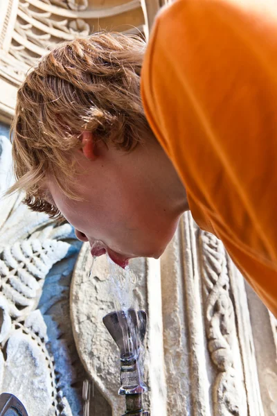 Мальчик пьет воду на общественном фонтане — стоковое фото