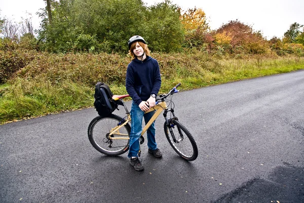 Jeune garçon avec le vélo en tournée par la pluie — Photo