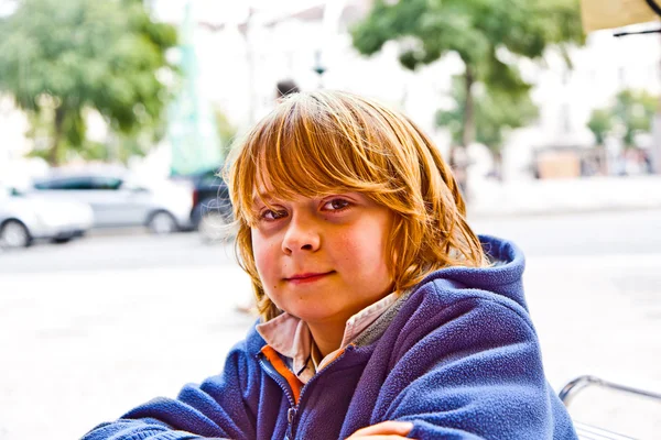 Niño con el pelo largo y los ojos marrones se ve muy seguro de sí mismo y feliz —  Fotos de Stock