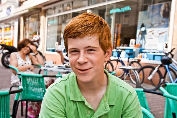 Niño con el pelo rojo se ve feliz y amigable sentado en una o —  Fotos de Stock