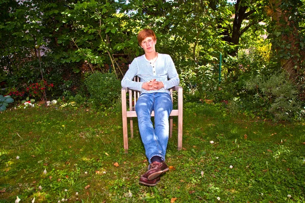 Rapaz amigável sentado em uma cadeira no jardim verde — Fotografia de Stock