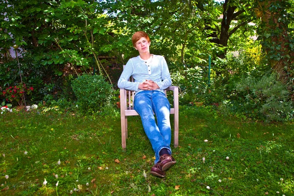 Trevlig pojke sitter på en stol i den gröna trädgården — Stockfoto