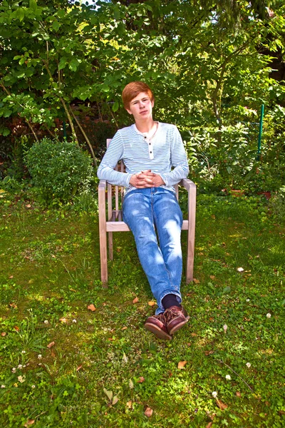 Φιλικό αγόρι κάθεται σε μια καρέκλα στον καταπράσινο κήπο — Φωτογραφία Αρχείου