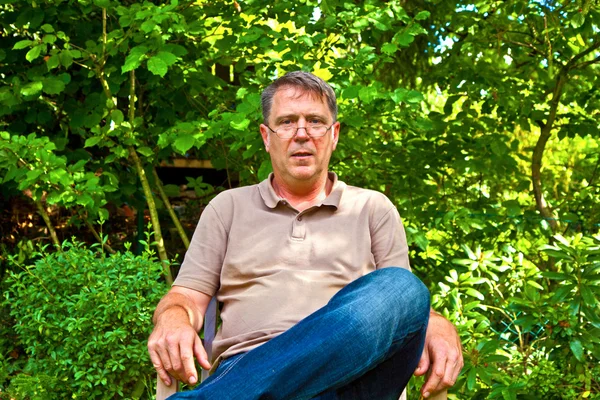 Přátelský člověk sedí ve své zahradě pod stromem — Stock fotografie