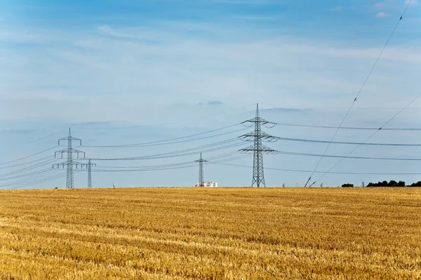 Tower for electricity in beautiful landscape with golden fields — Stock Photo, Image