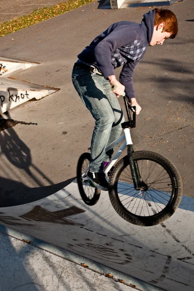 Giovane ragazzo con i capelli rossi sta saltando con la sua moto allo skate park — Foto Stock