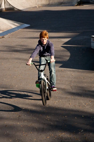 Jeune garçon aux cheveux roux saute avec son vélo au skate park — Photo