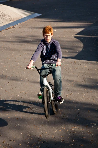 Jeune garçon aux cheveux roux saute avec son vélo au skate park — Photo
