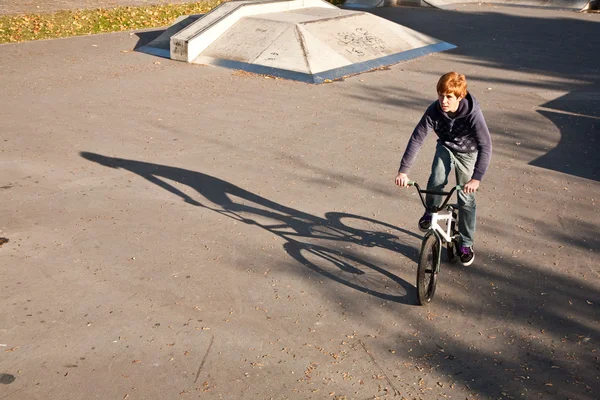 Niño con el pelo rojo está saltando con su bicicleta en el parque de skate —  Fotos de Stock