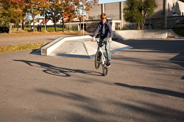 Menino com cabelo vermelho está pulando com sua bicicleta BMX no parque de skate — Fotografia de Stock