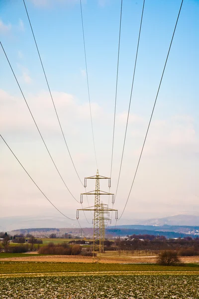 Electrical tower in winter on flatland with marks of car in field — Stock Photo, Image