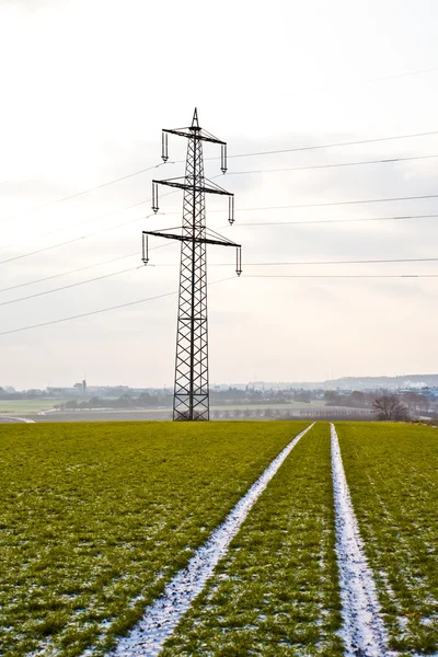 Strommast im Winter auf flachem Land mit Spuren von Auto im Feld — Stockfoto