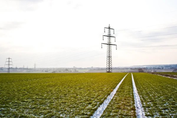 Torre eléctrica en invierno en llanura con marcas de coche en el campo — Foto de Stock