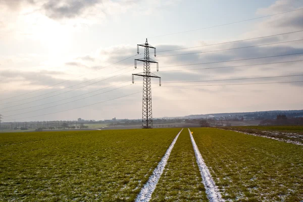 Torre elétrica no inverno na planície com marcas de carro no campo — Fotografia de Stock