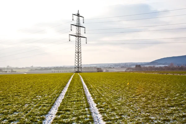 Torre eléctrica en invierno en llanura con marcas de coche en el campo — Foto de Stock