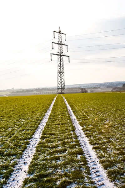 Elektriska tower i vinter på slättlandskap med markerar bil i fältet — Stockfoto