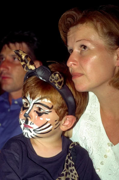 El niño y la madre están viendo una actuación, el niño tiene un maquillaje de gato y mira v — Foto de Stock