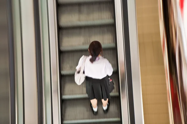 Student on the moving staircase in school dress — Stock Photo, Image