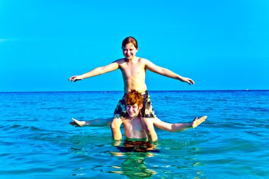 Brothers are enjoying the clear warm water at the beautiful beach and playi clipart