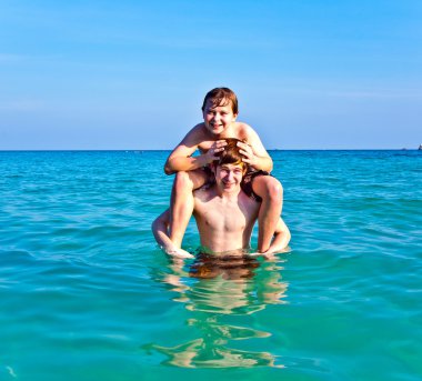Brothers are enjoying the clear warm water at the beautiful beach clipart