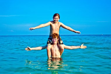 Brothers are enjoying the clear warm water at the beautiful beach clipart