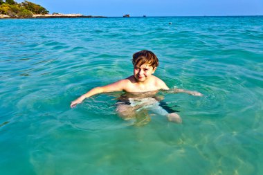 Young boy enjoys the clear water of the ocean clipart
