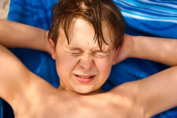 Netter kleiner Junge am Strand schließt wegen heller Sonnenstrahlen die Augen — Stockfoto